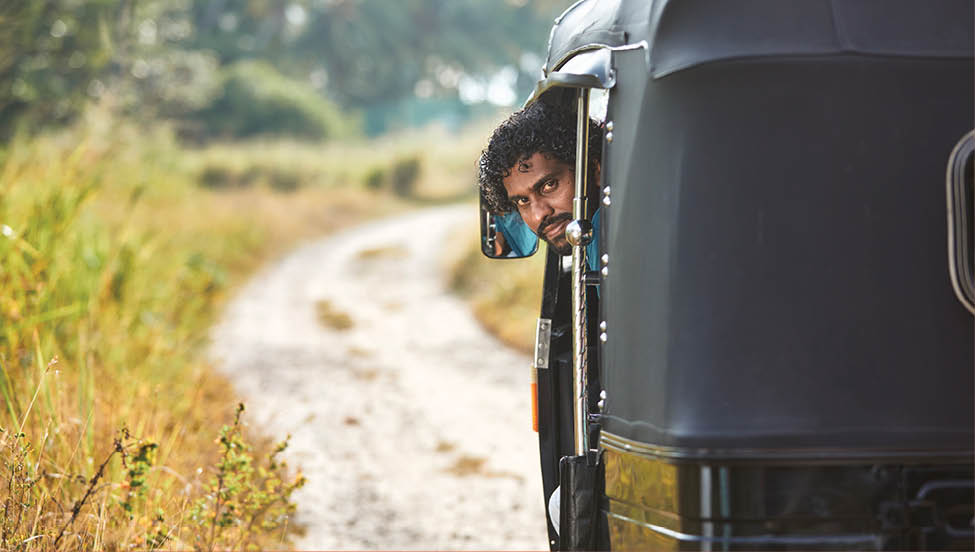 Portrait of tuk tuk driver on rural road. Popular three wheeled motorcycle in Sri Lanka. 